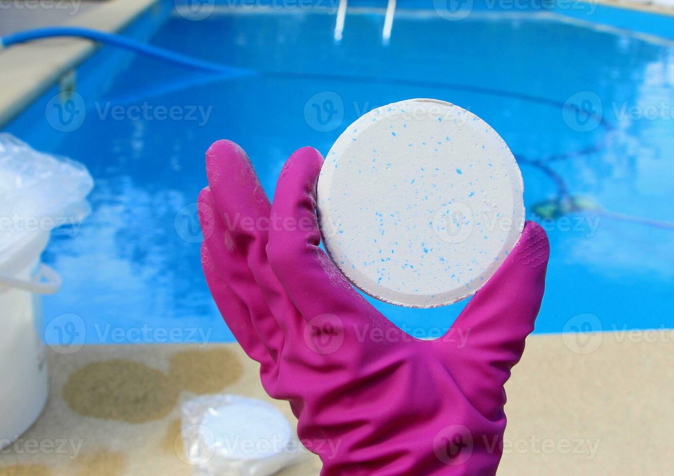 A white large chlorine tablet in the hand of a purple protective glove of a pool disinfection service worker. The beginning of the swimming season in the hot summer on vacation. photo