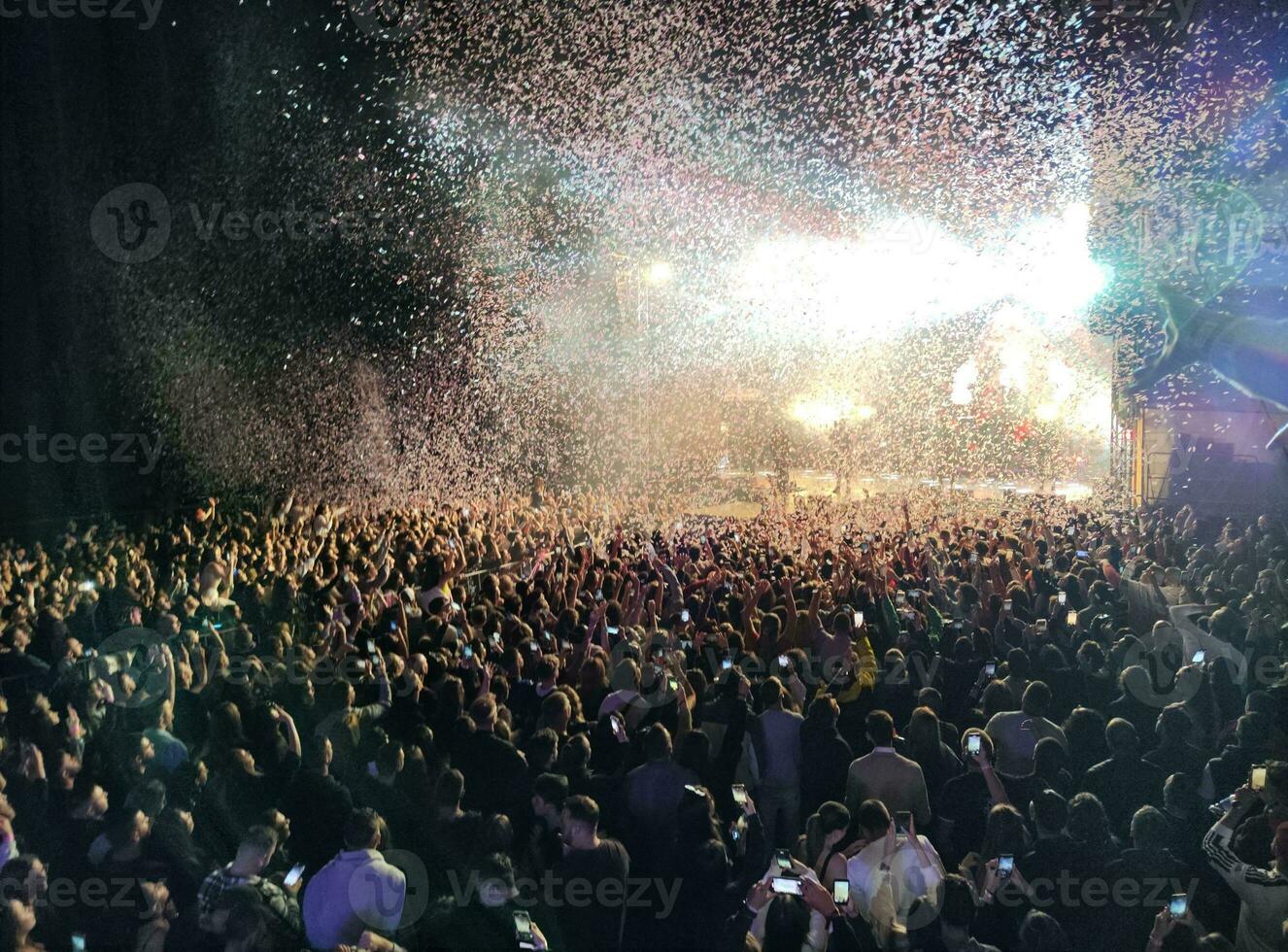 Concert with wig crowd with cell phones  bright lights and lots of confetti photo