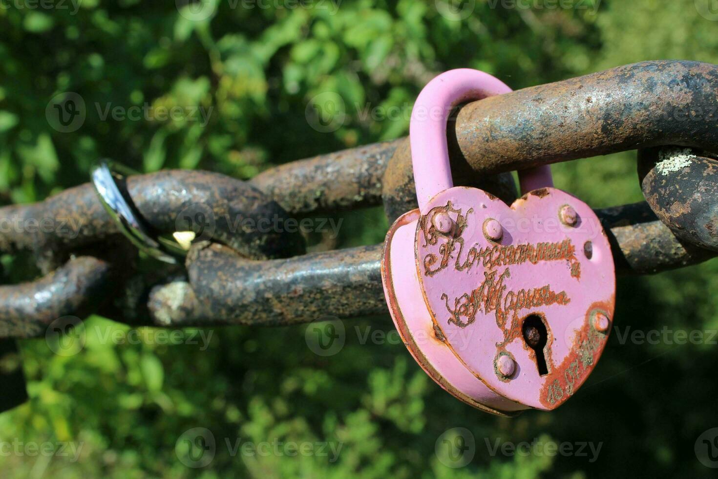 Pink love padlock attached to chain. Rusty lock with heart shape carved hanging outdoors. Valentines day, unity, memory concepts photo