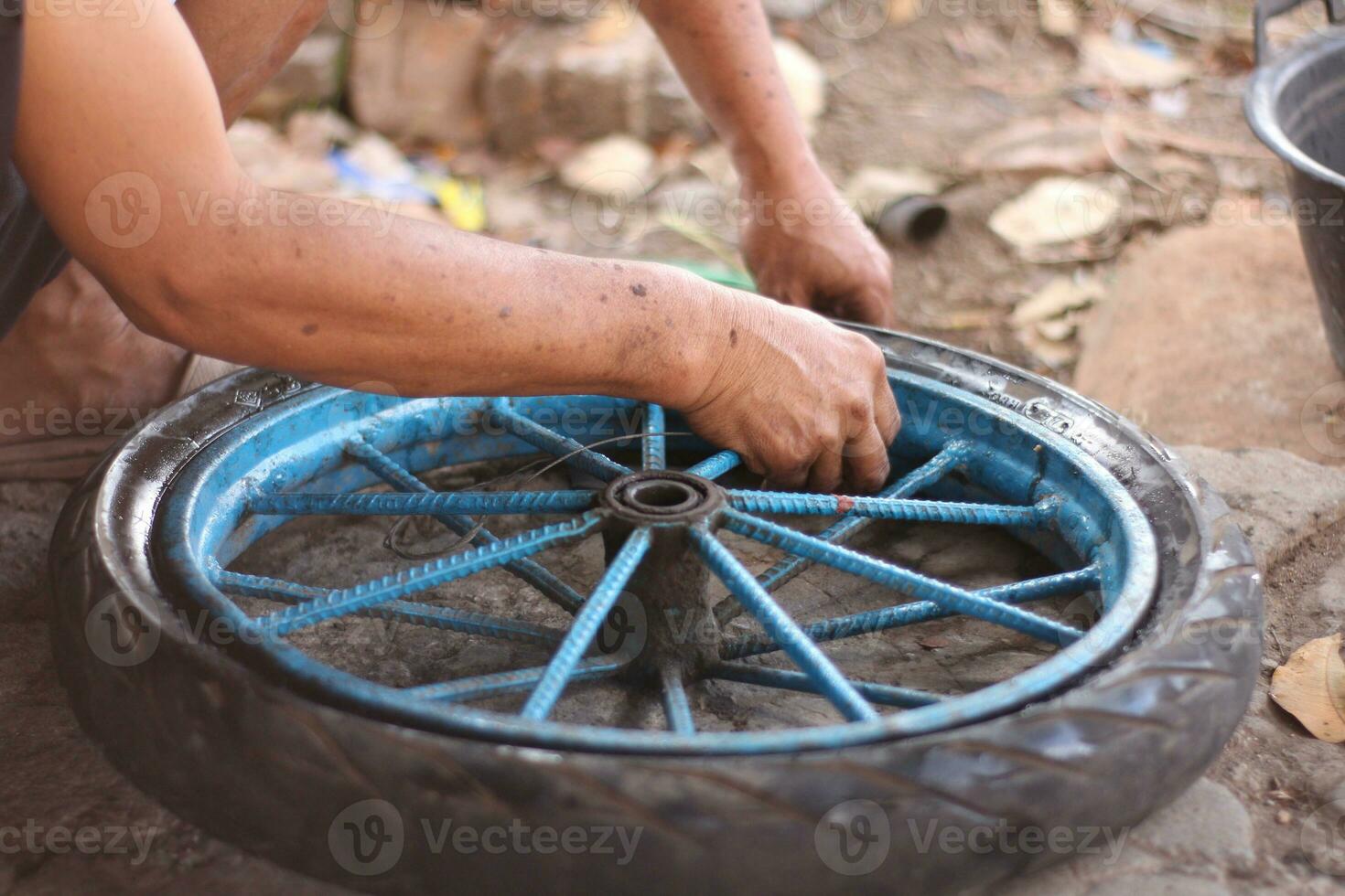 An Indonesian service worker is changing the tire of a bicycle cart manually photo