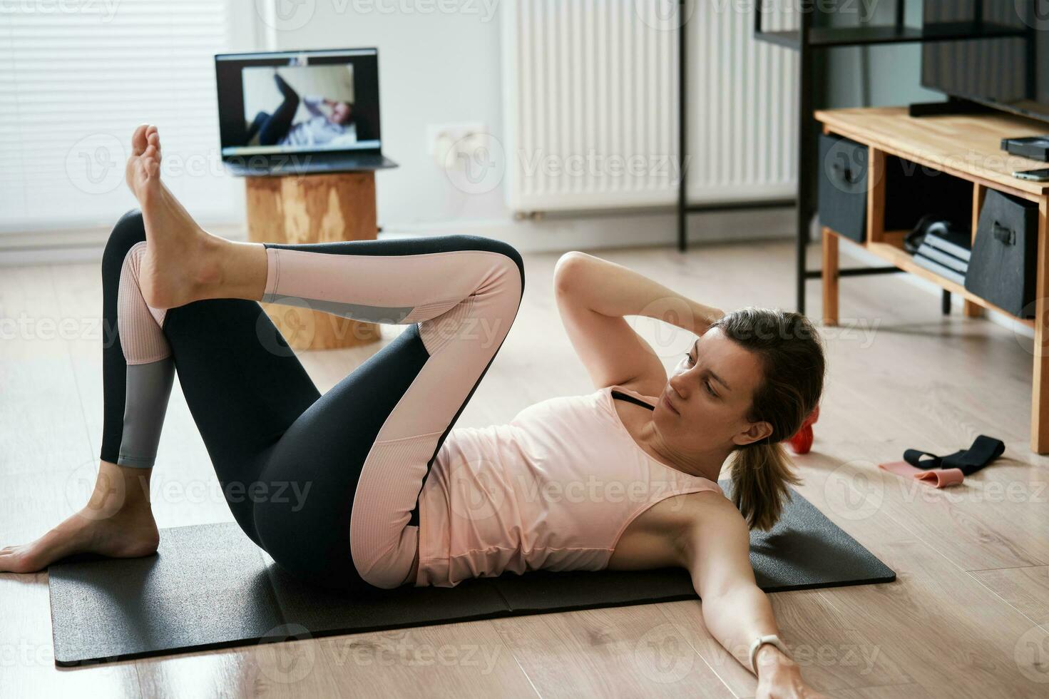 Woman in sports clothes does fitness cardio exercises at home, using laptop photo