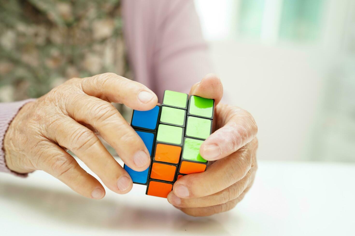 Bangkok, Thailand - May 15, 2022 Asian elderly woman playing Rubik cube game to practice brain training for help dementia prevention and Alzheimer disease. photo