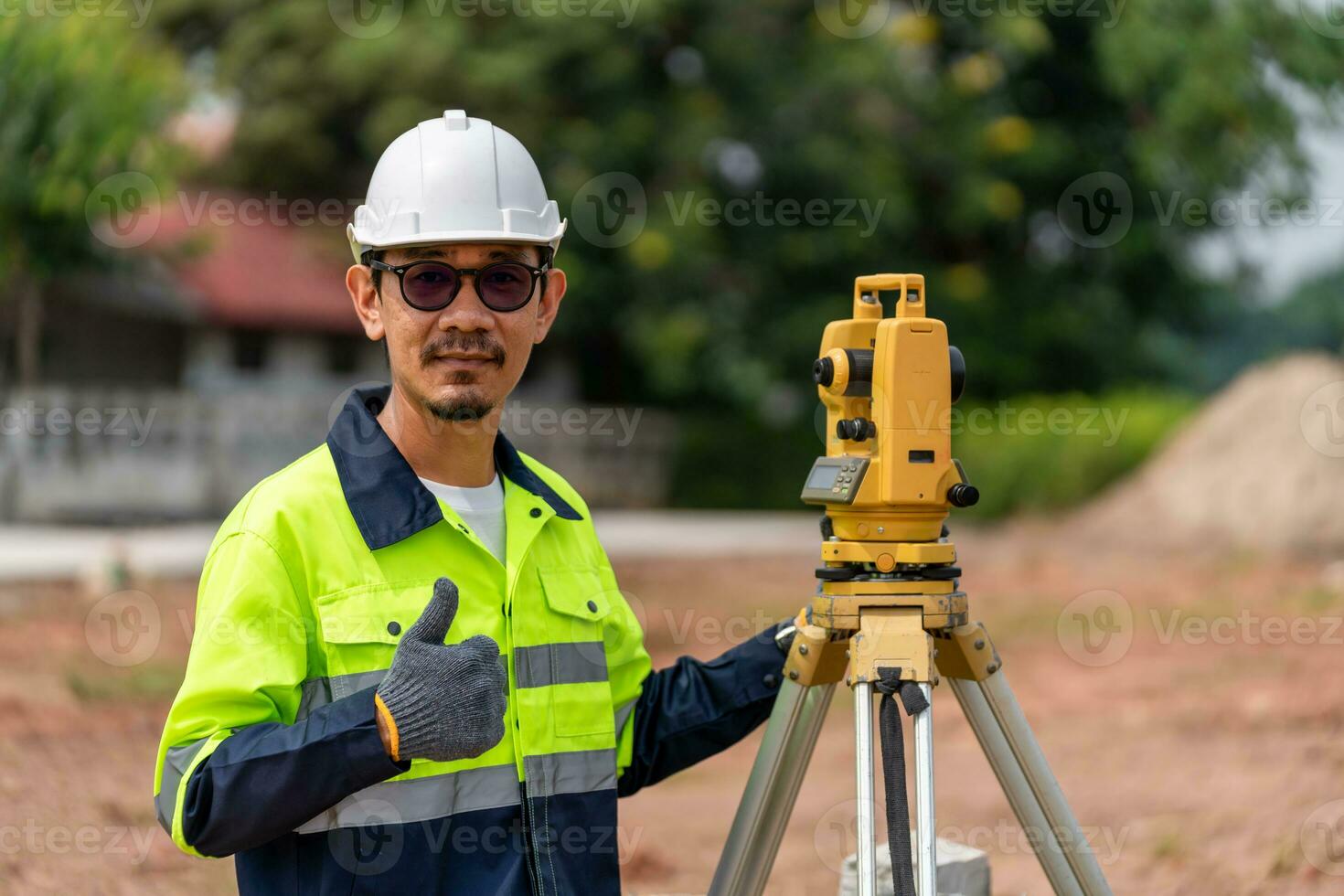 asiático topógrafo civil ingeniero pulgares arriba con equipo en el construcción sitio. foto