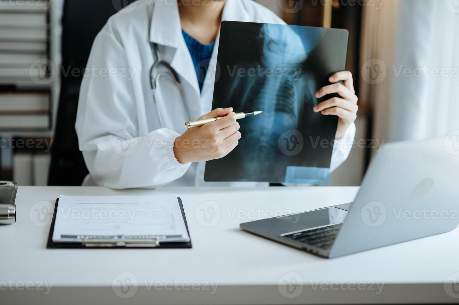 Young Asia lady doctor in medical uniform with stethoscope using computer laptop and tabler talking video conference call with patient at desk in health clinic or hospital. photo