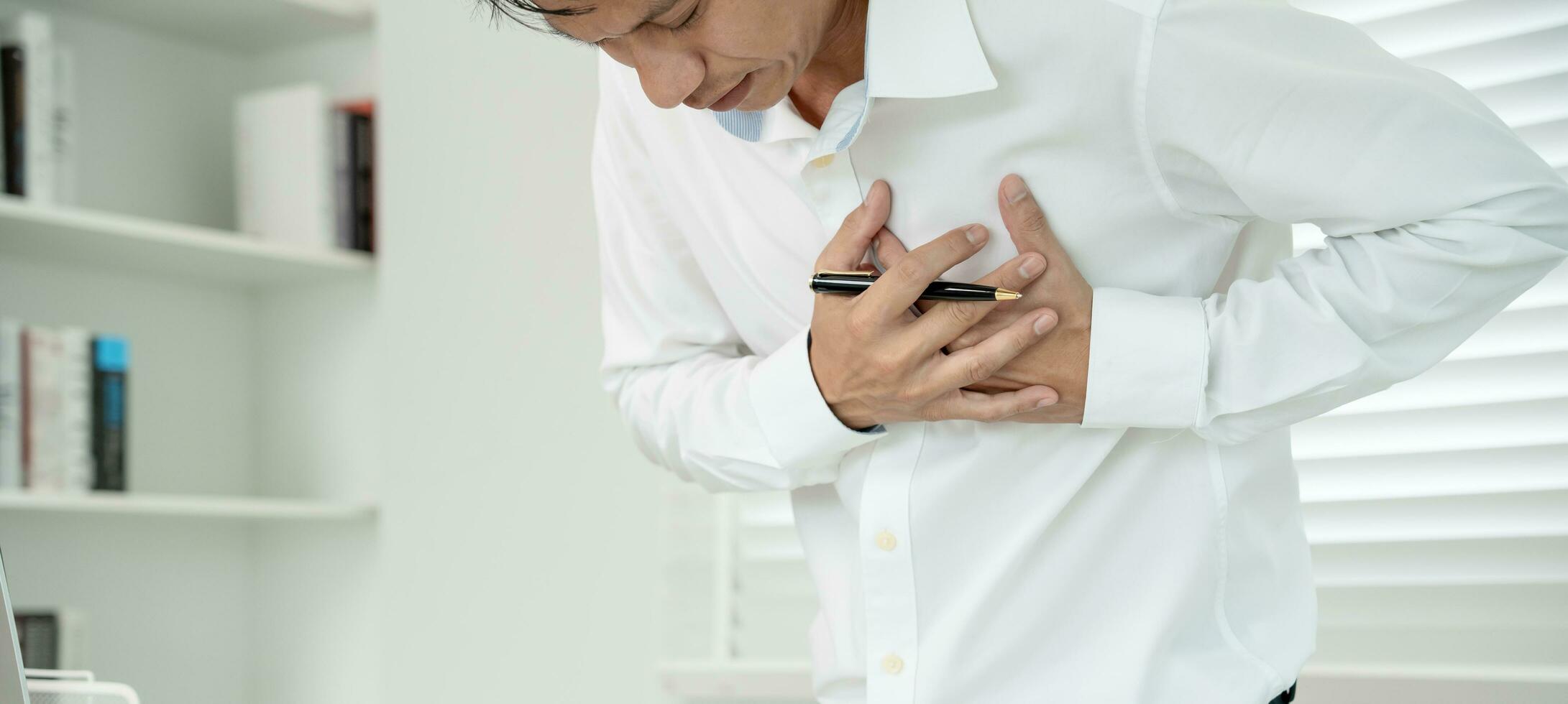 hand hold chest with heart attack symptoms, asian man working hard have chest pain caused by heart disease, leak, dilatation, enlarged coronary heart, press on the chest with a painful expression photo