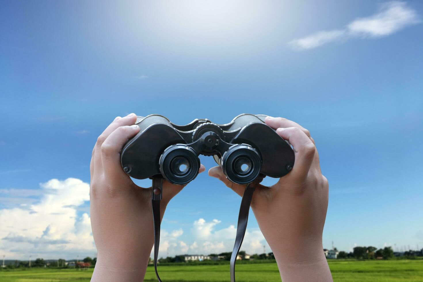 Binoculars holding in hands against blue and cloudy sky background. photo