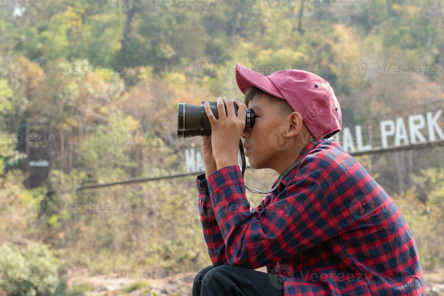 asian boys holds binoculars and local national park map, resting and reading information in map near sling bridge of local national park during nature and summer camp of them, teens' activity concept. photo