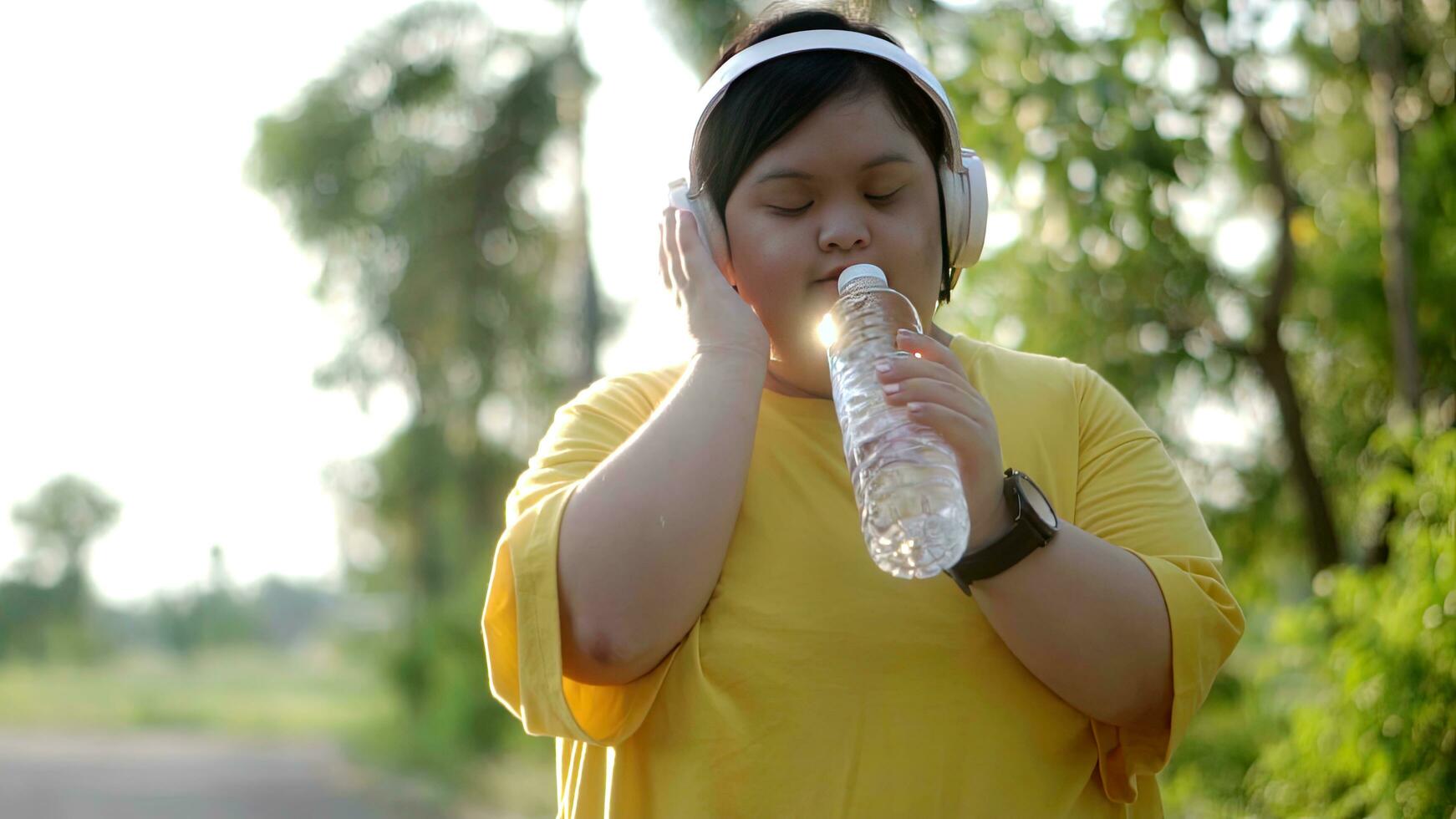 Asian girl with down syndrome in headphones uses water bottle as microphone to sing while exercising in the park. photo