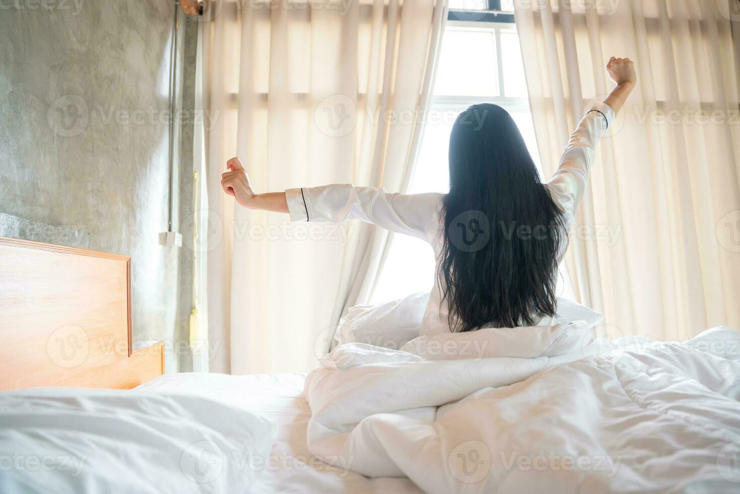 Happy Asian Young Girl Greets New Day with Warm Sunlight Flare, Sun shines on her from the big window. photo