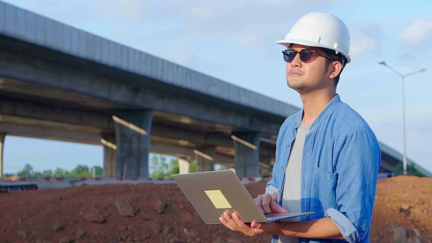 Asian civil engineer using laptop is inspecting construction project a road expressway that is done at construction site. photo