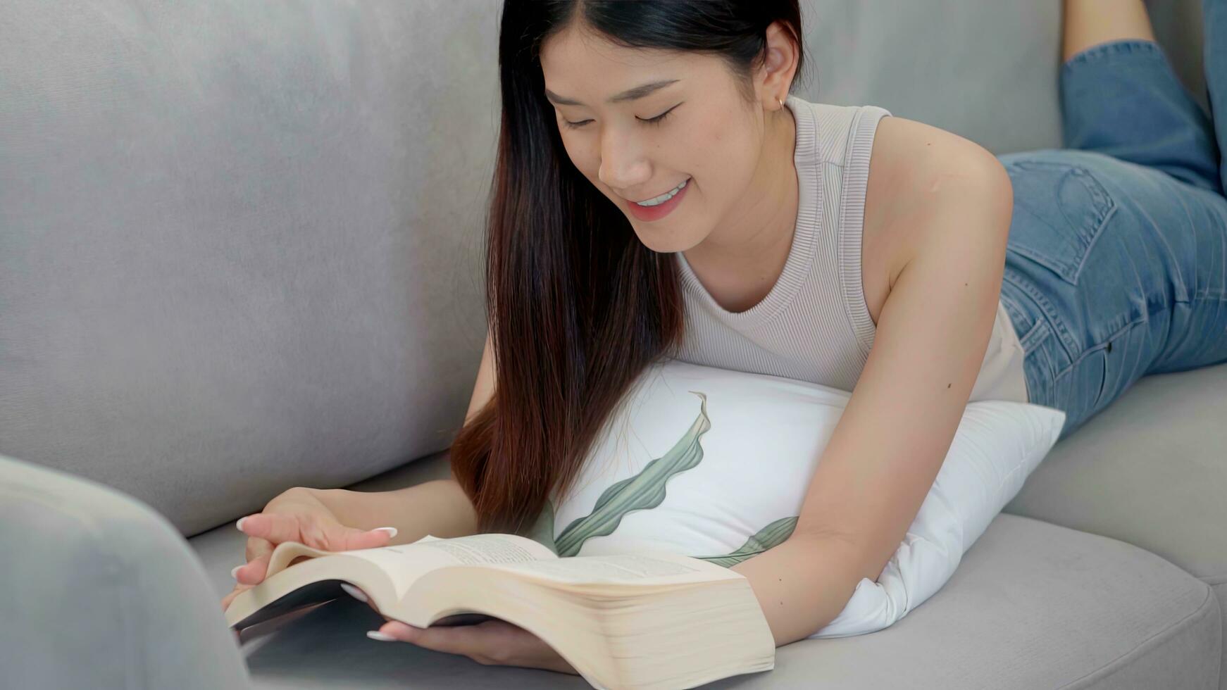 hermosa asiático joven mujer leyendo libro en sofá a hogar. foto