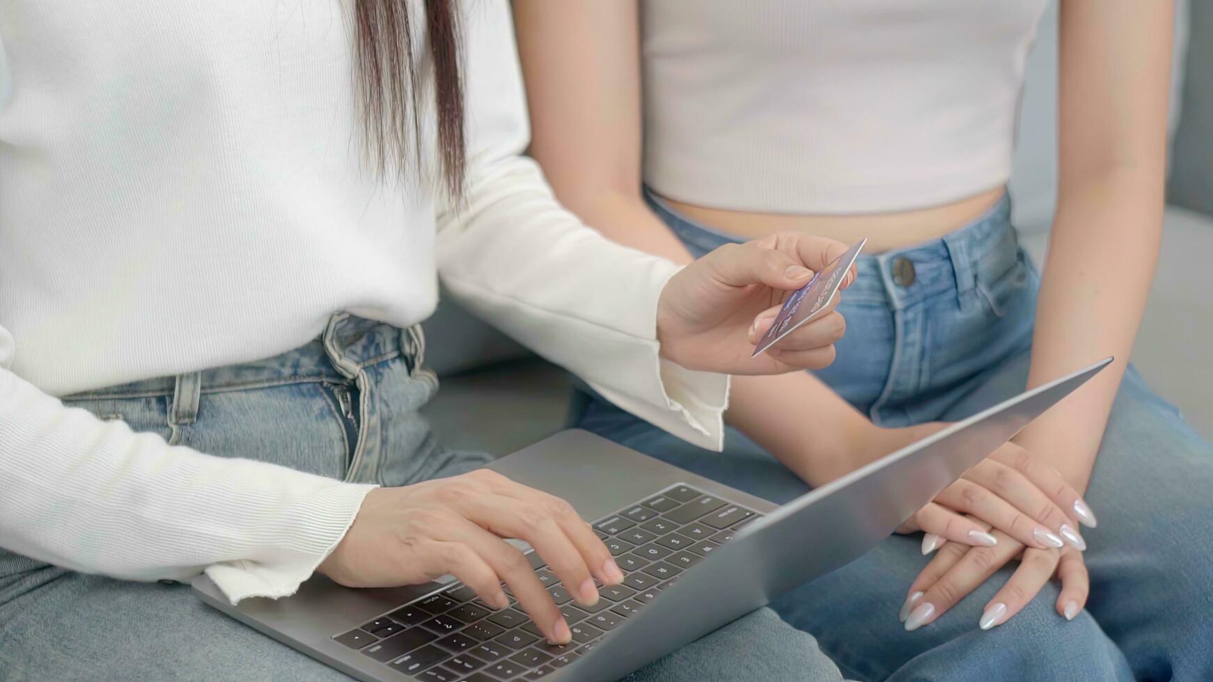 Close up hand two asian women using online shopping credit cards via their laptops on sofa at home. Online success buy sale. photo