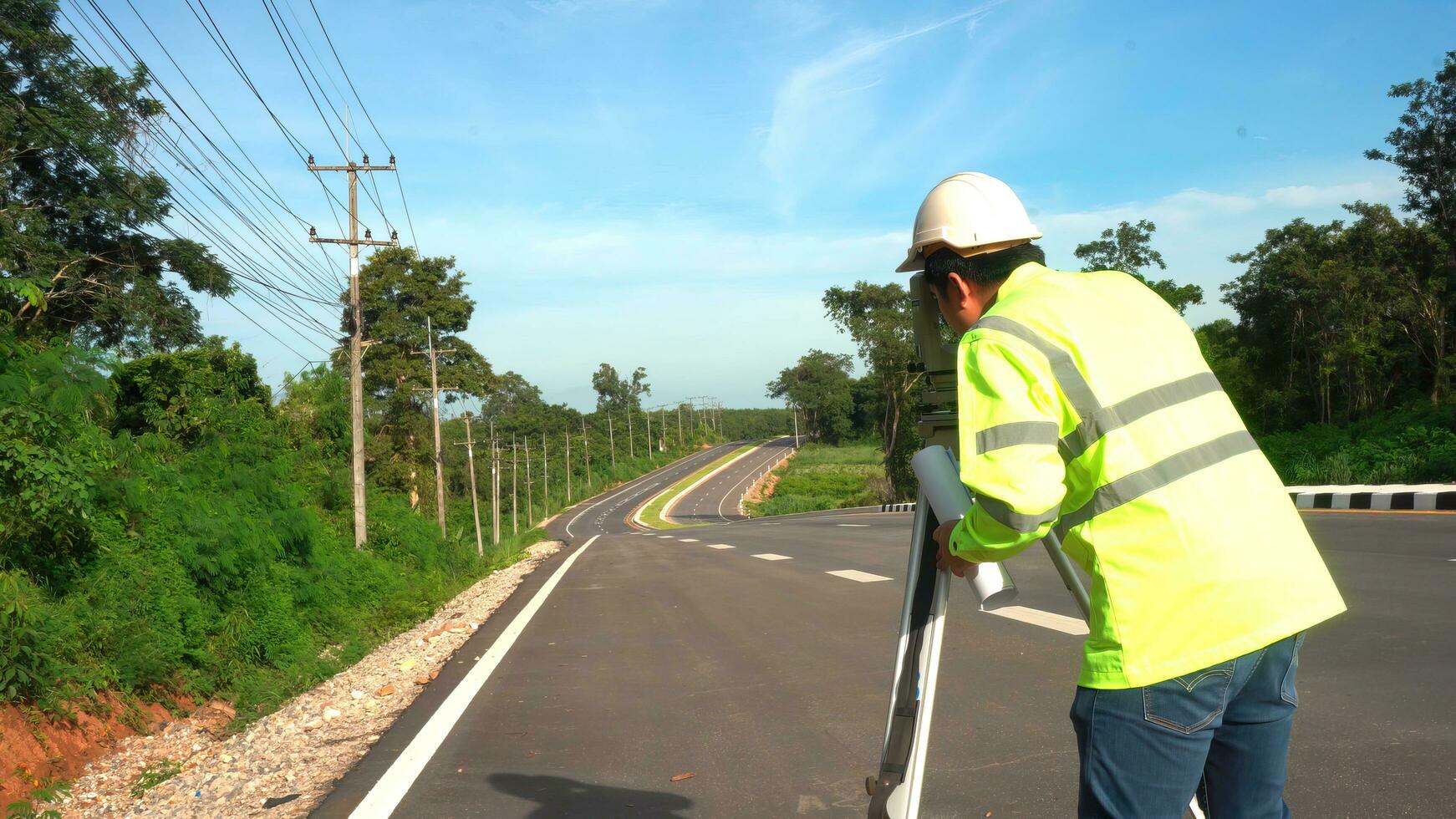 topógrafo ingeniero con teodolito en la carretera autopista durante el soleado día con la carretera en antecedentes. foto