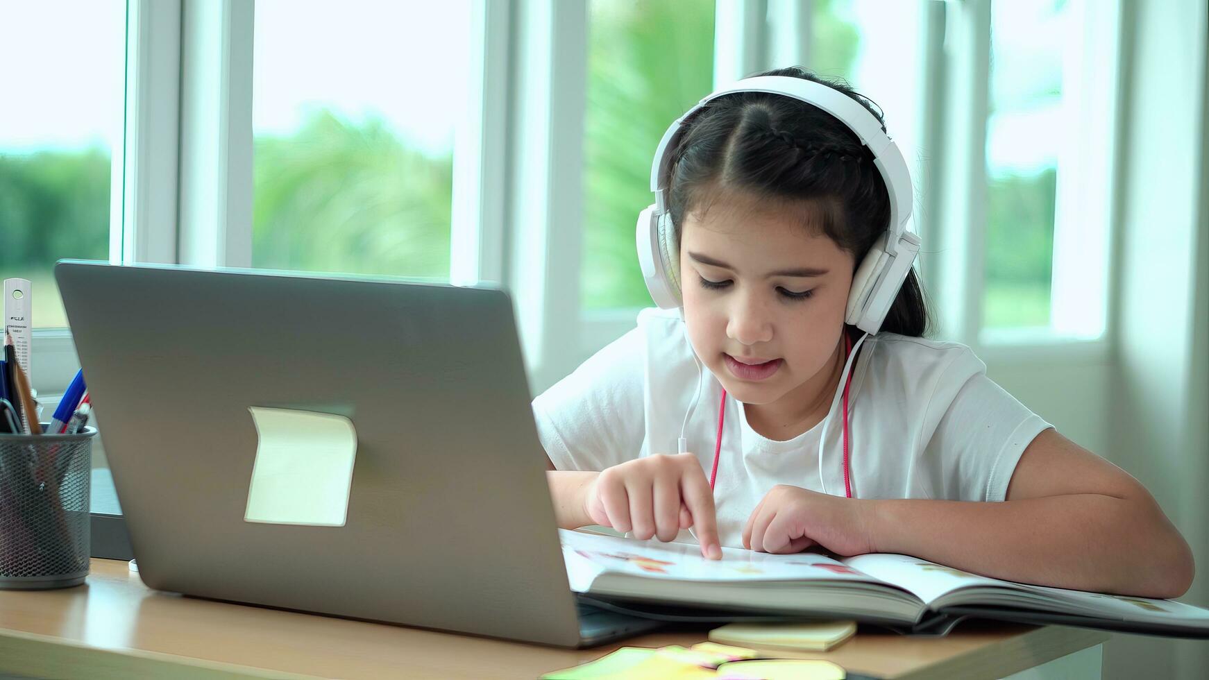 Young girl reading a book attentively. Cute young girl reading on computer screen sitting in living room. Kid playing game on laptop or doing homework. photo