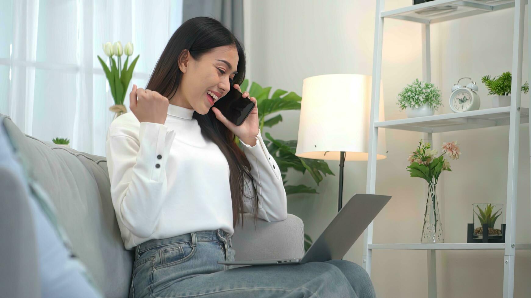 Smiling asian woman making phone call, working on laptop at home. Freelance success consept. photo