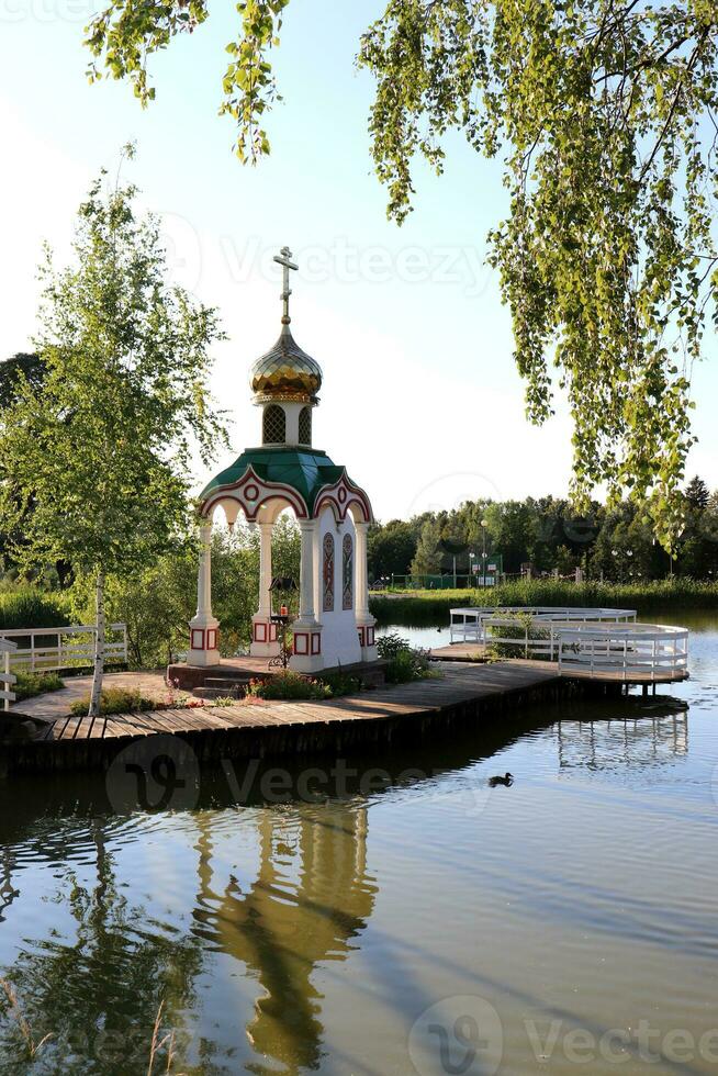 Chapel of the Royal Passion-Bearers in Demyanovo on a summer evening. Stone chapel-canopy over the mosaic icon of the Royal Passion-Bearers on a small island of Demyanovsky Pond photo