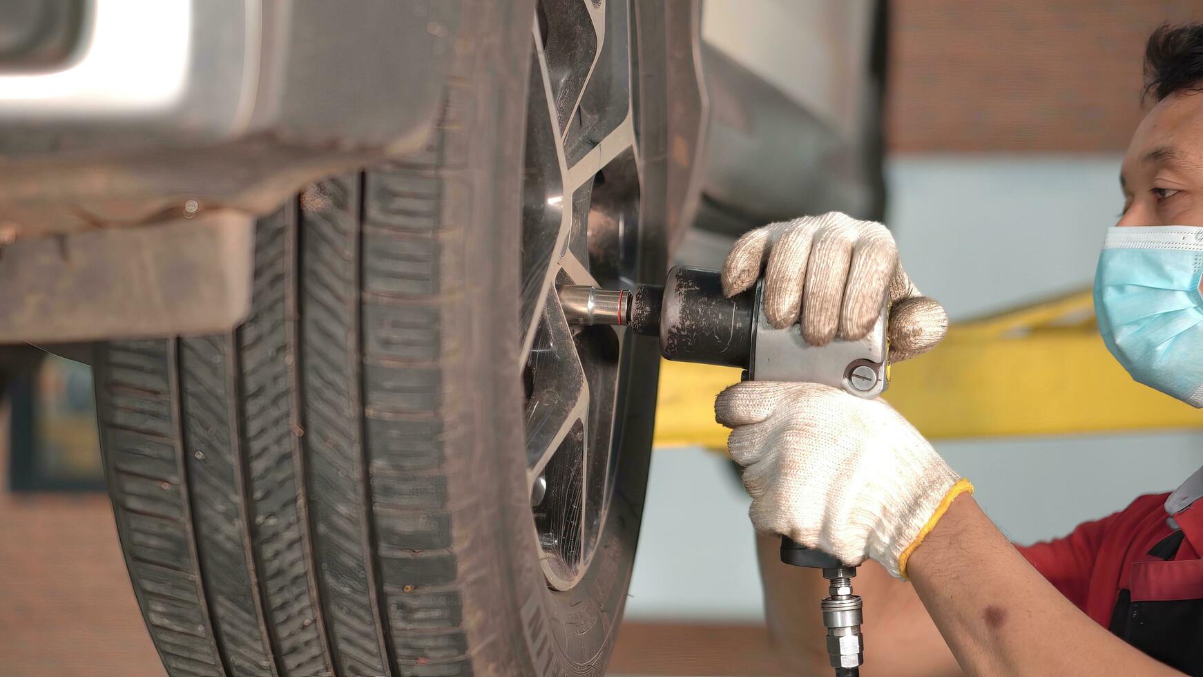 Asian man car mechanic replacing a car tire in garage workshop. . Auto service, Car-care center removes the wheel, Repair and maintenance of the car in service. photo