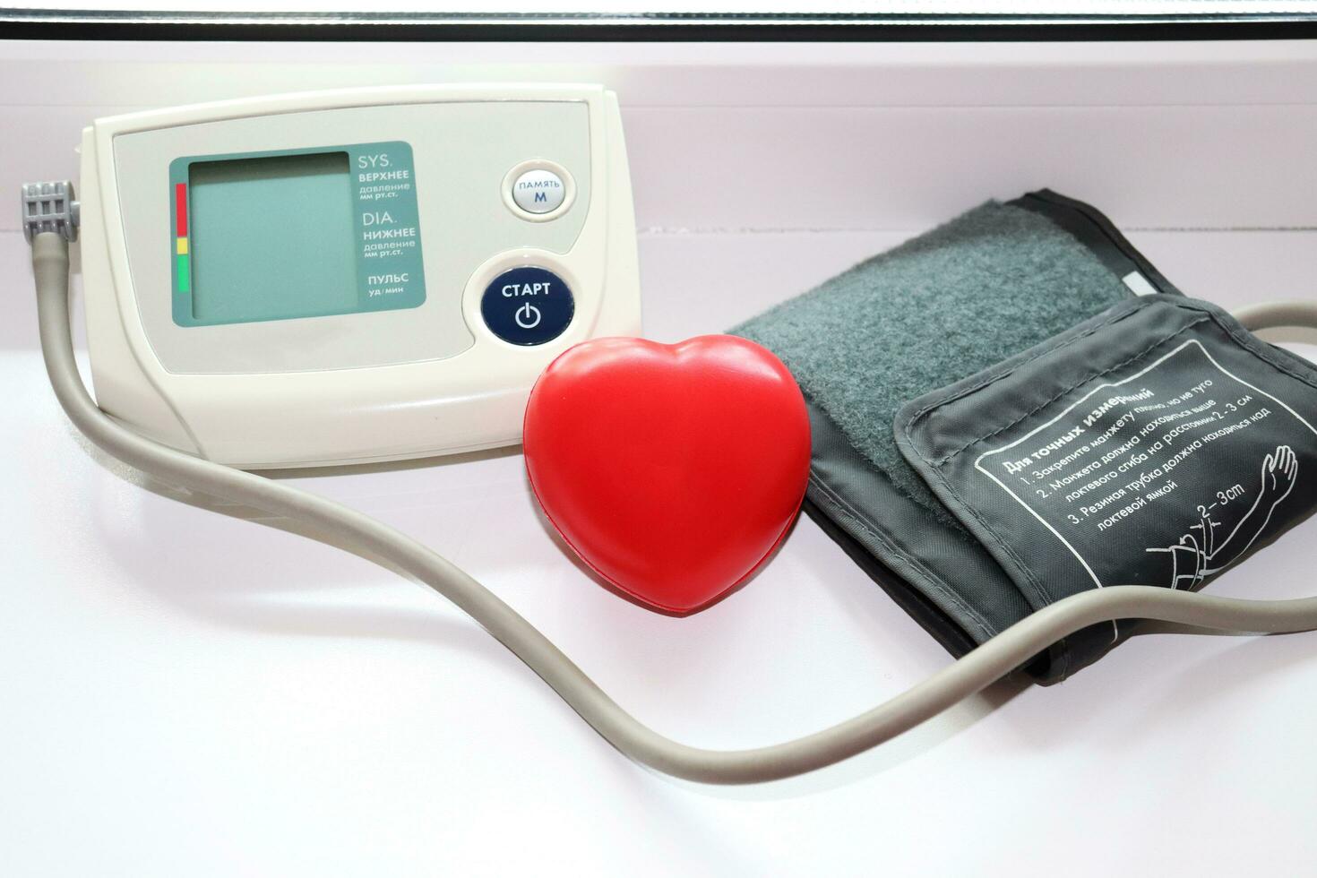 automatic portable blood pressure monitor - turned off device by the window and rubber hand trainer in the shape of a heart photo