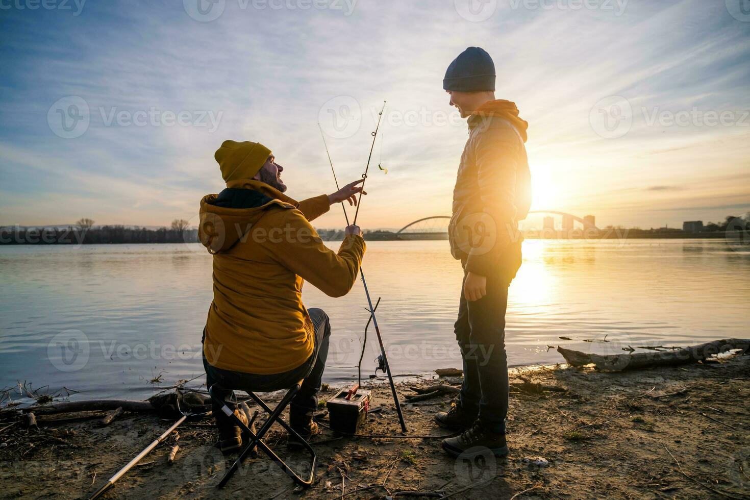 Father and son are fishing on winter day. River fishing. Teenage boy is learning to fish. photo