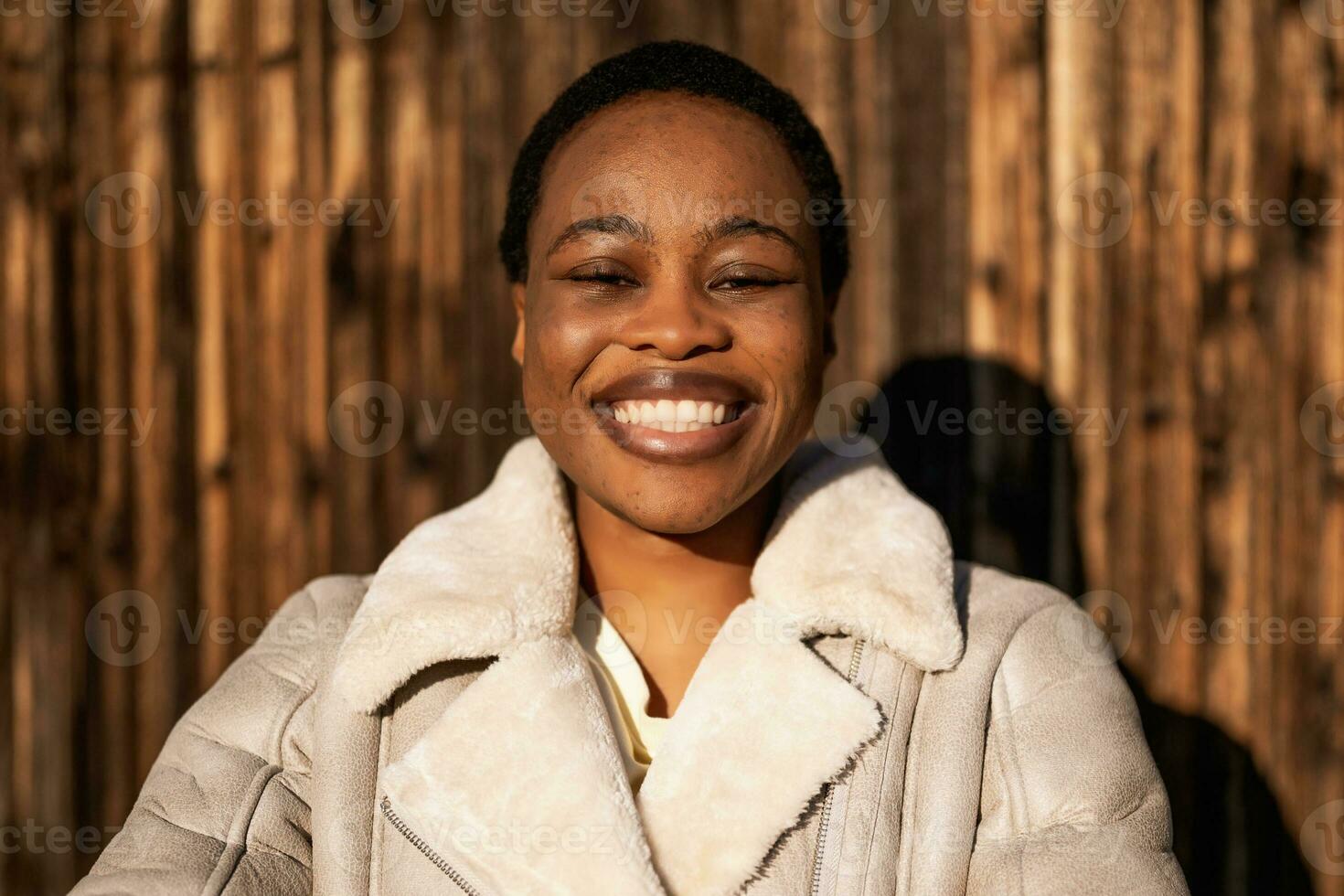 Outdoor portrait of happy african-american woman. She is standing in front of wooden wall and smiling. photo