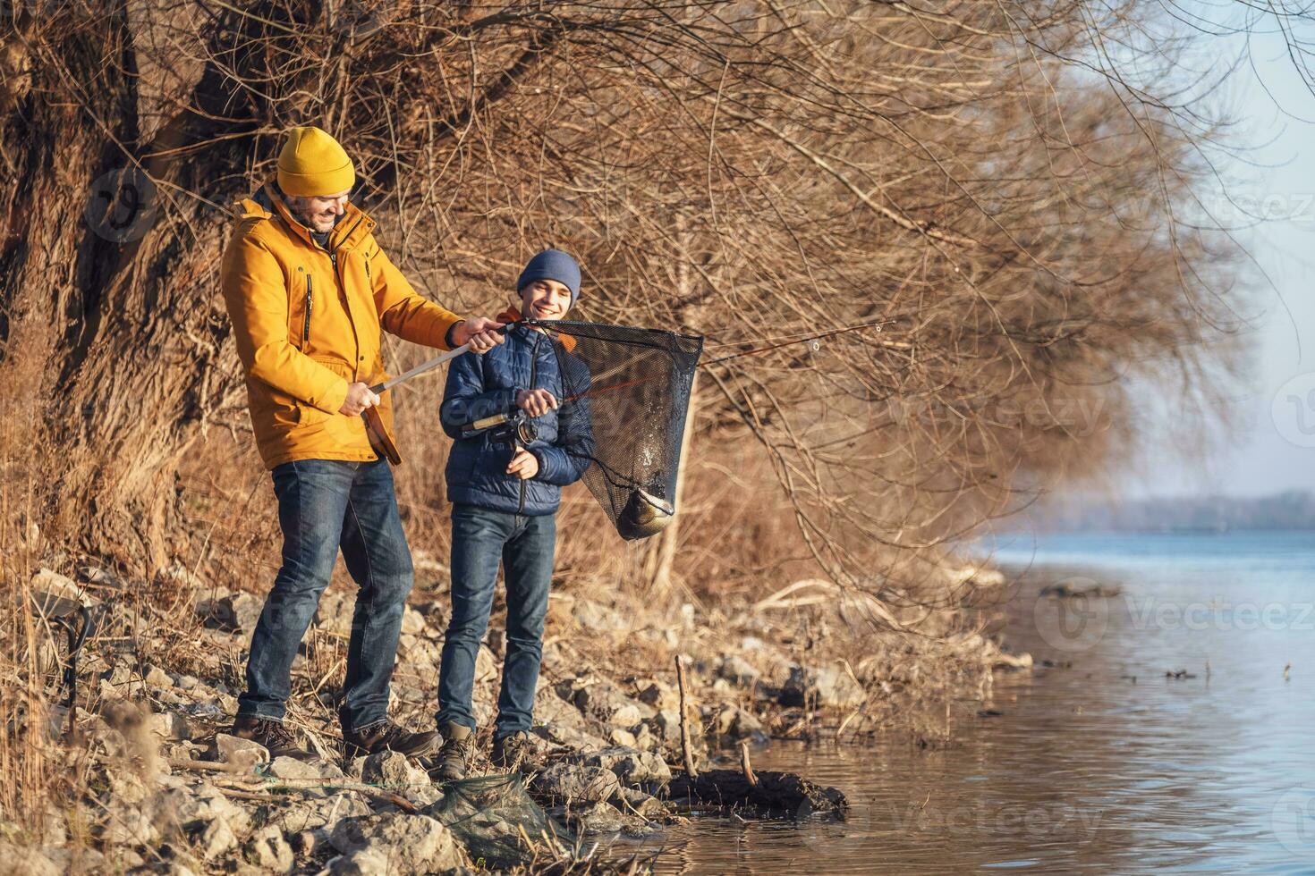 Father and son are fishing on sunny winter day. They caught a fish and are holding it in a landing net. photo