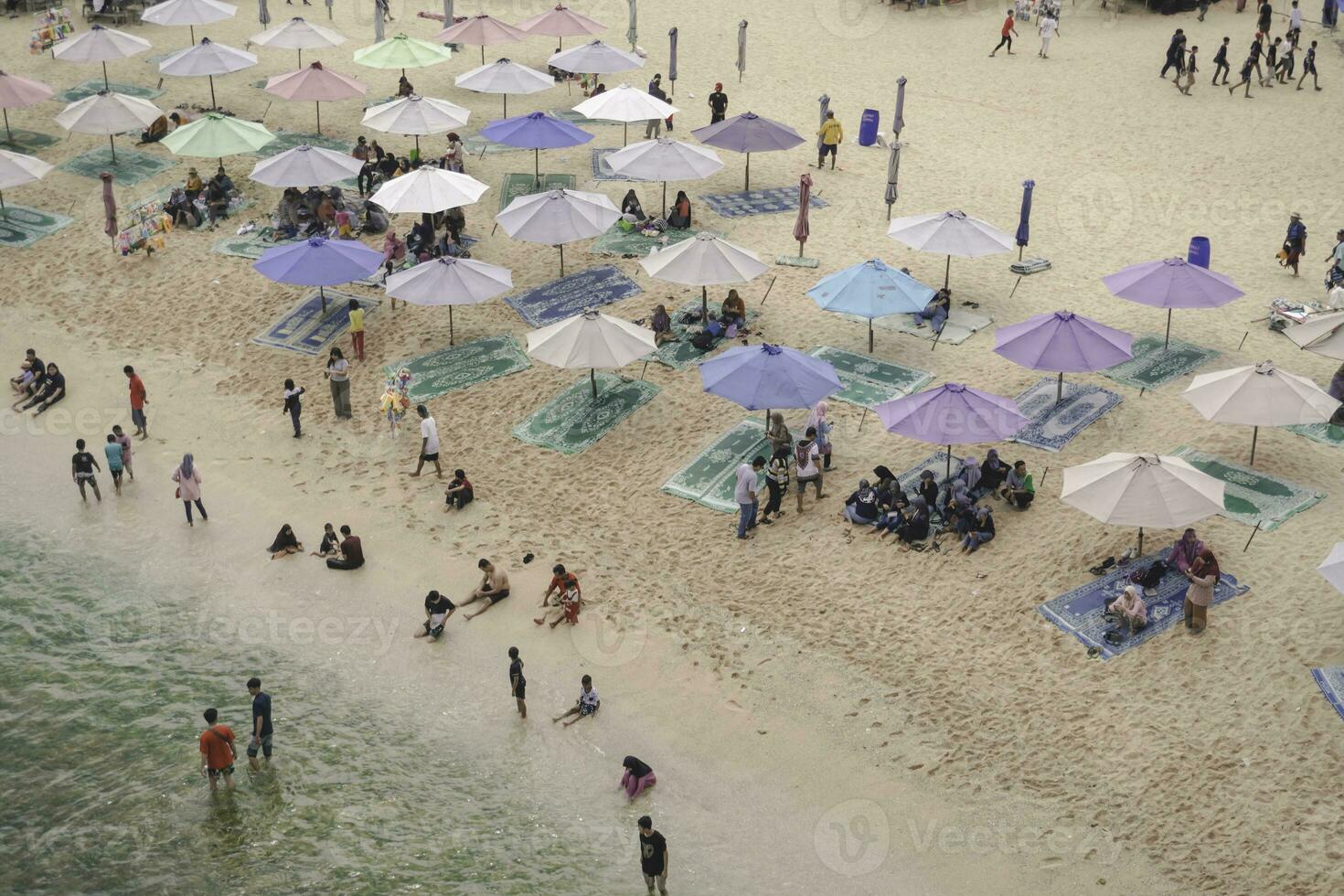 Aerial drone view of Holiday In Ndrini Beach, Yogyakarta, Indonesia with ocean, beach, umbrellas, and people. photo