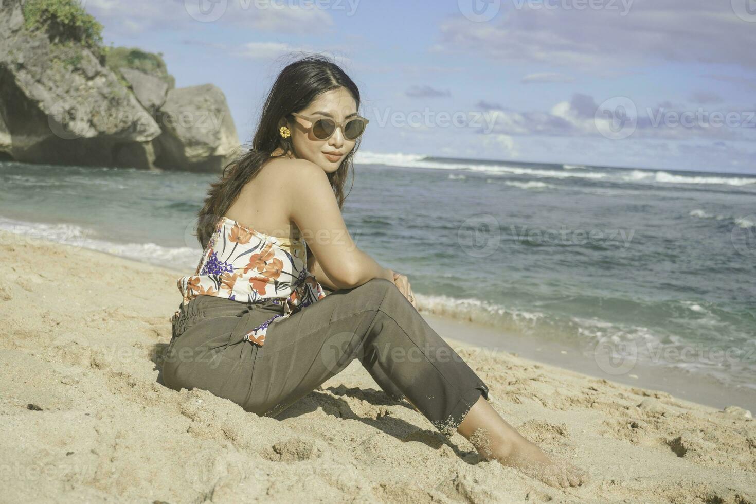 joven asiático mujer sentar en el playa arena. retrato sexy asiático dama de viaje y relajante en el verano con tropical naturaleza. foto