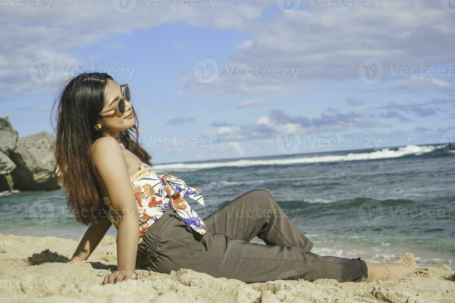 Young Asian woman sit on the beach sand. Portrait sexy Asian lady traveling and relaxing in the summer with tropical nature. photo