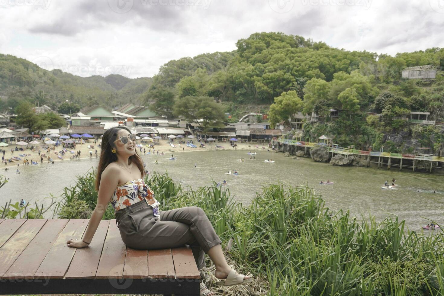 Young Asian girl sitting on the edge of cliff above the sea hearing wind by herself. Holiday concept photo