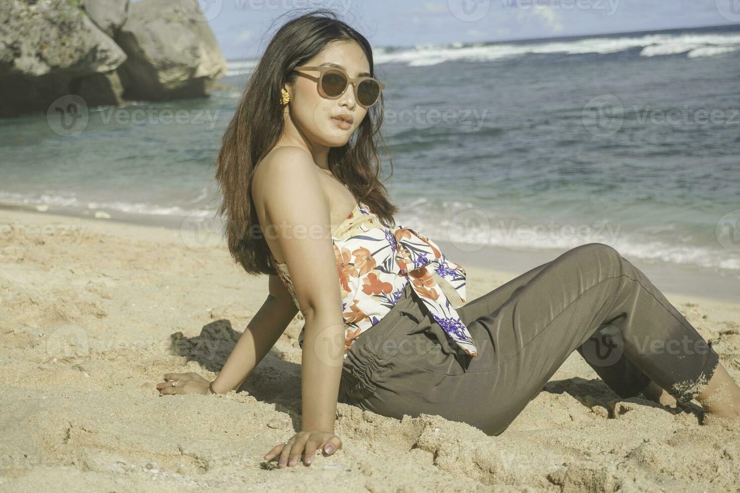 Young Asian woman sit on the beach sand. Portrait sexy Asian lady traveling and relaxing in the summer with tropical nature. photo