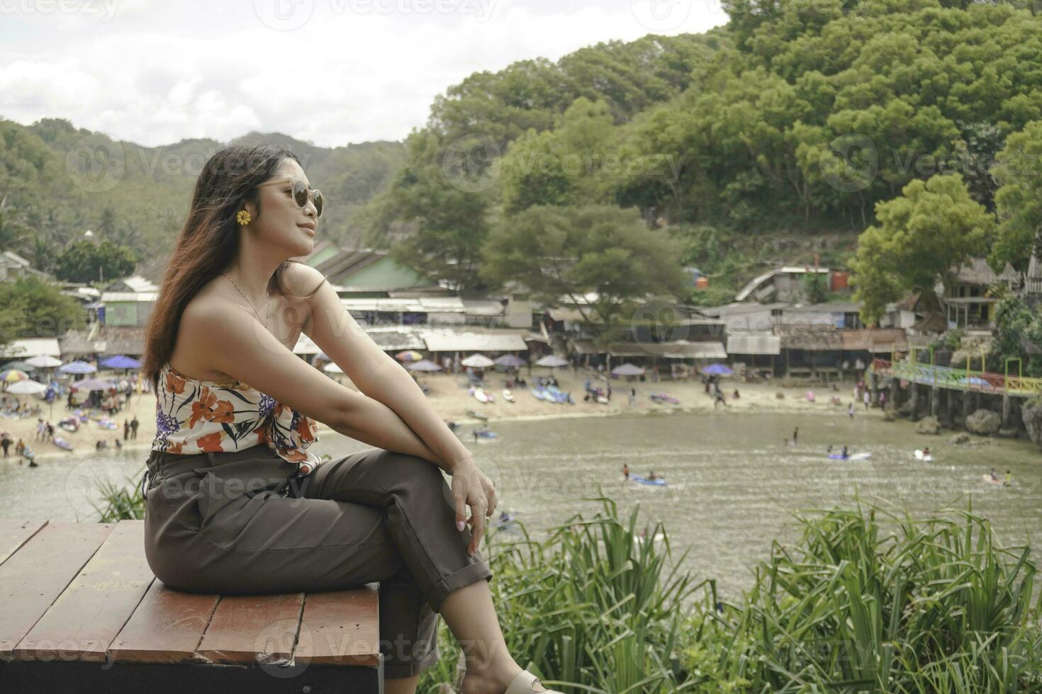 Young Asian girl sitting on the edge of cliff above the sea hearing wind by herself. Holiday concept photo