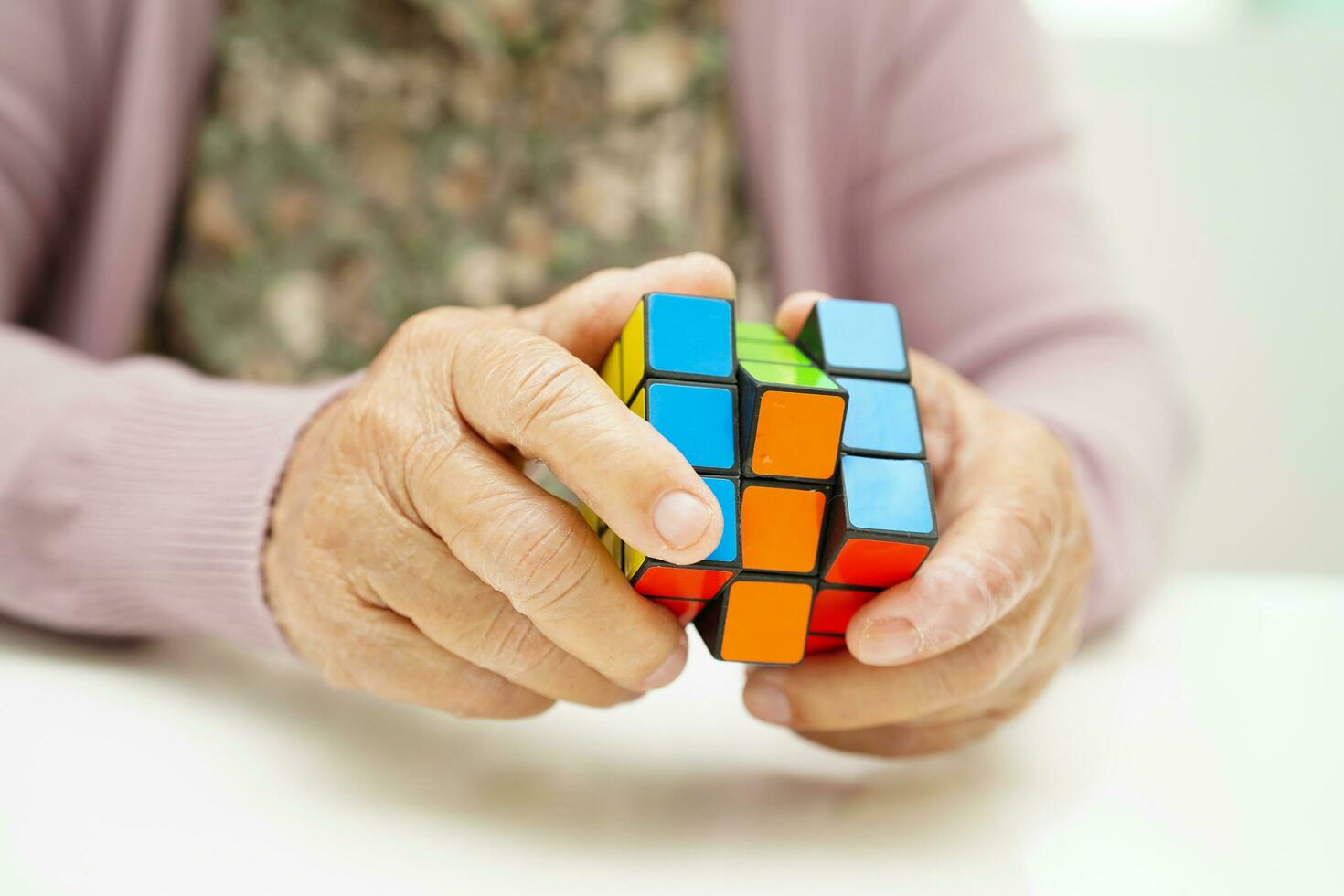 Bangkok, Thailand - May 15, 2022 Asian elderly woman playing Rubik cube game to practice brain training for help dementia prevention and Alzheimer disease. photo