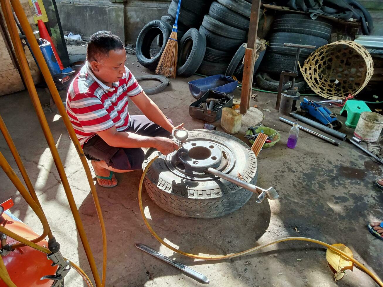 East Denpasar, Bali, Indonesia - June 8, 2023  An Asian man is patching a car tire in a tire repair shop on Cok Agung Tresna street photo