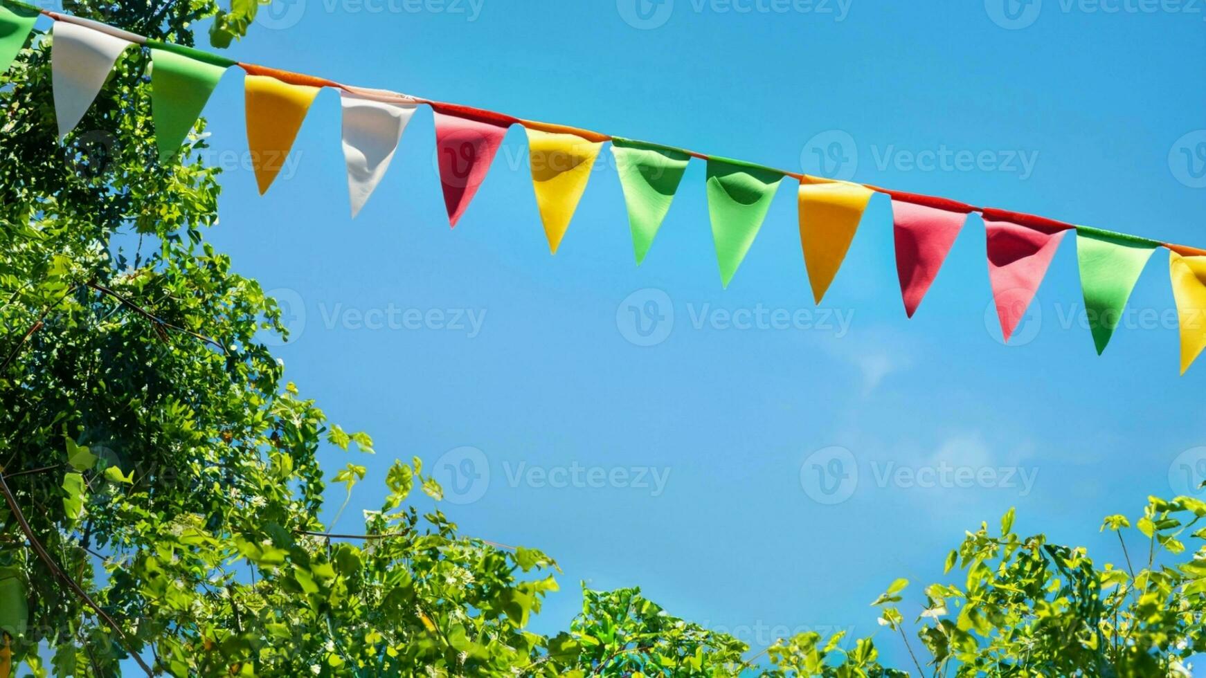 colorful pennant string decoration in green tree foliage on blue sky, summer party background photo