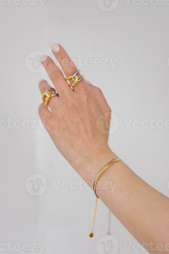 Woman hand wearing Snake Chain bracelets and Interlocked Golden and Silver Rings set against a white background. Beautiful valentine's gift. photo