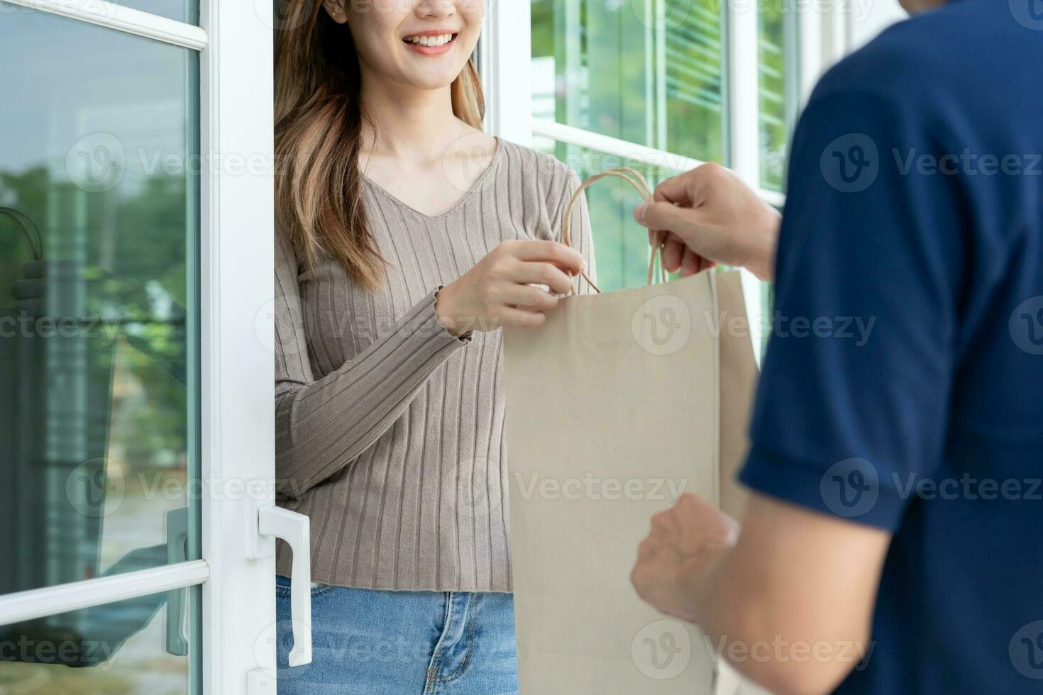 Happy smiling Asian woman receives paper bag parcel of food from courier front house. Delivery man send deliver express. online shopping, paper container, takeaway, postman, delivery service, packages photo