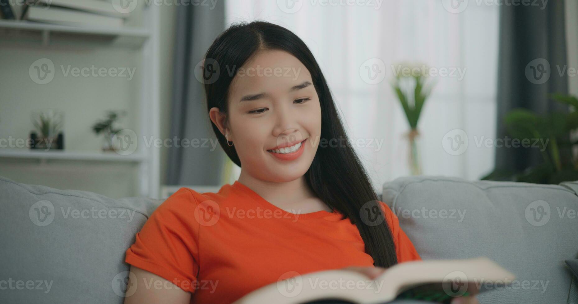 asiático mujer leyendo un libro mientras sentado en el sofá foto