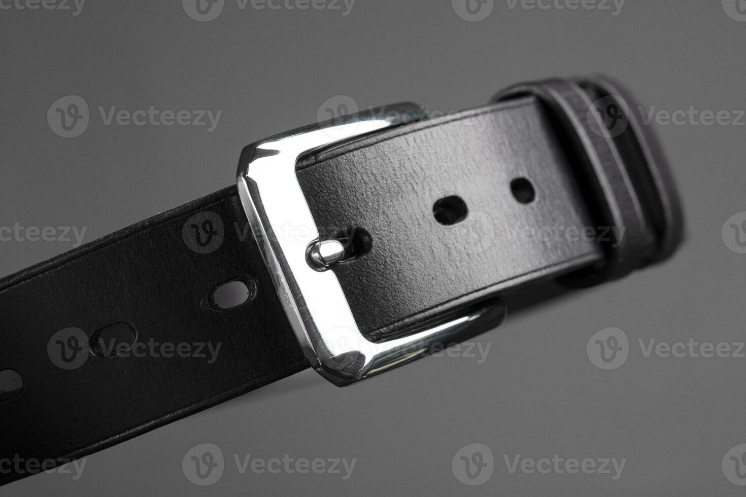 Part of a black leather belt with a metal buckle close-up on a gray background. photo