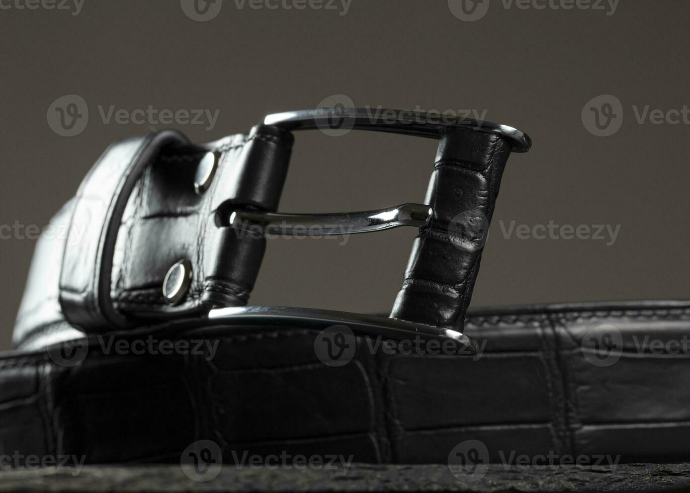 Black leather belt with a metal plaque close-up on a gray background. photo