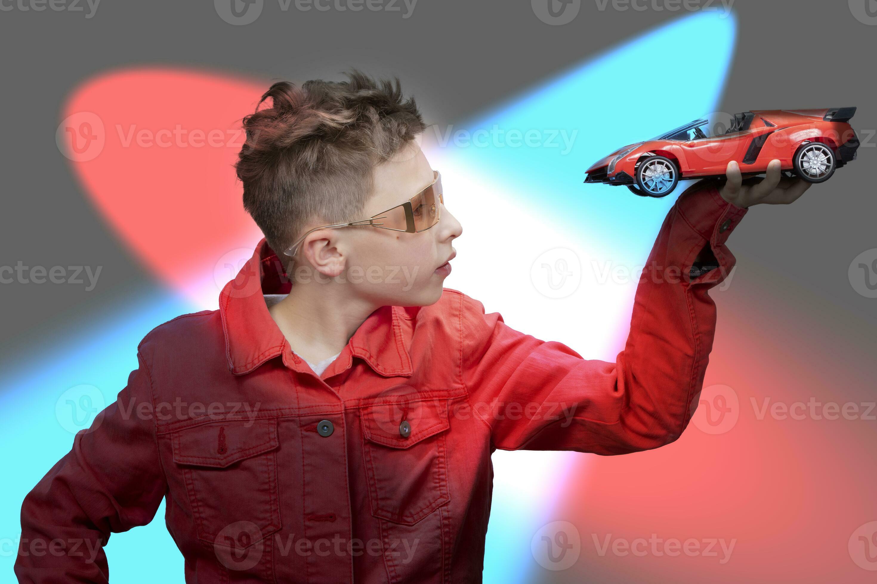 A fashionable boy is holding a toy car in his hands, on a multi-colored  studio background. A beautiful child with glasses dreaming of a real car.  Dreams of a child about racing. 28671584 Stock Photo at Vecteezy