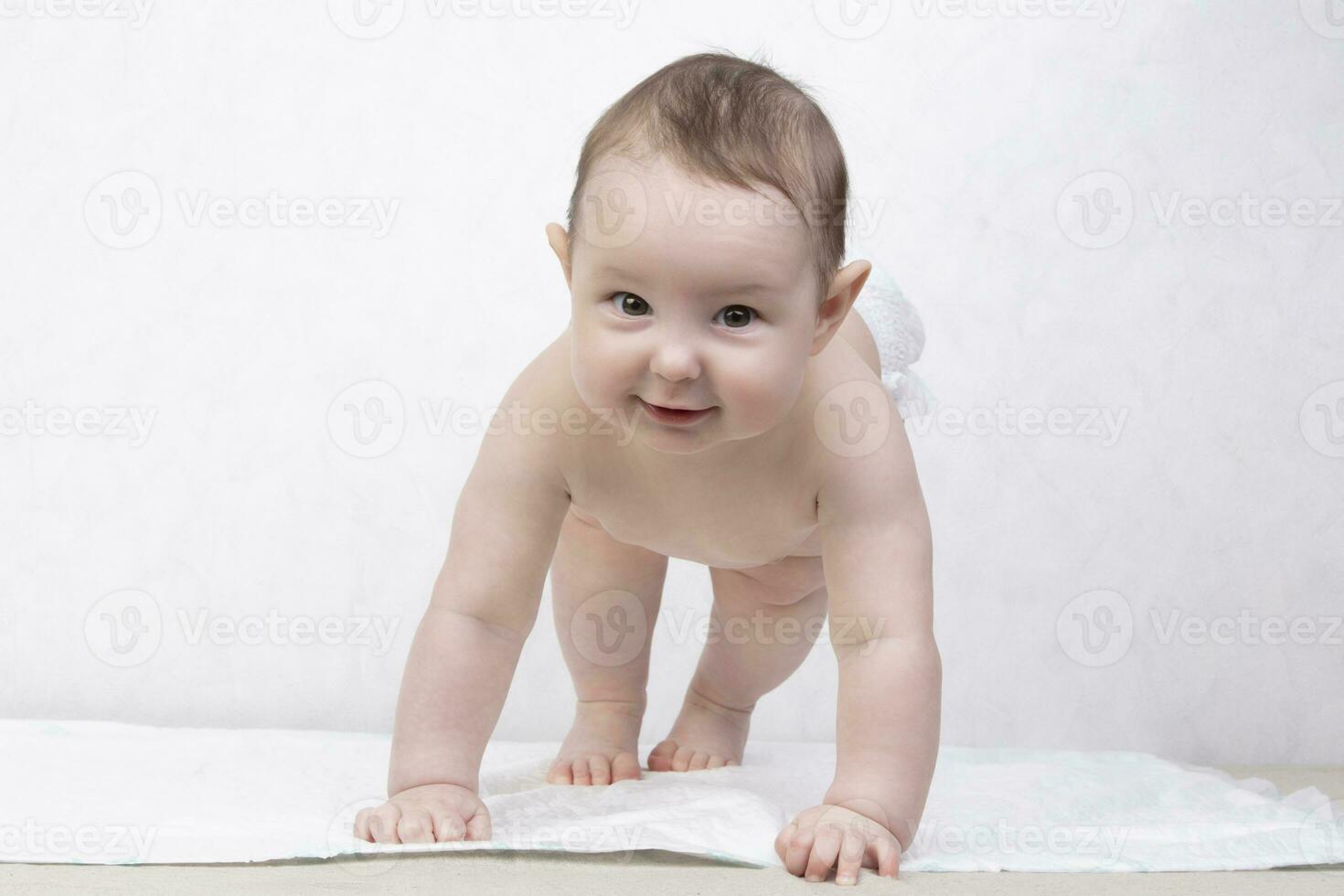 Kid with a smile on a white background. A happy six month old boy crawls on the bed and laughs. Conceptual photo of fatherhood and motherhood.