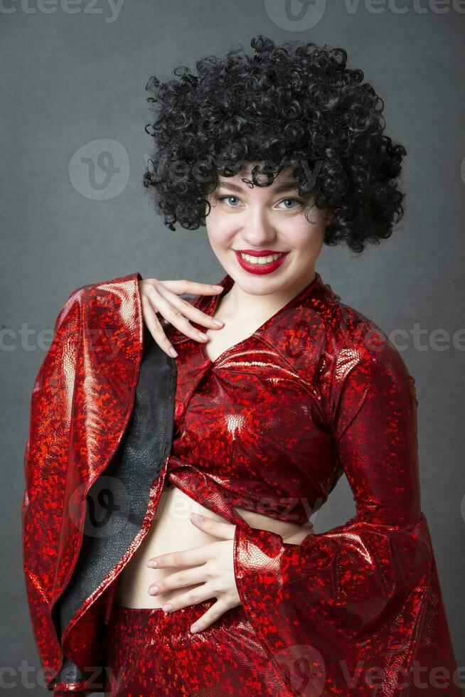 Excited woman in an afro wig on a gray background. Disco girl. photo