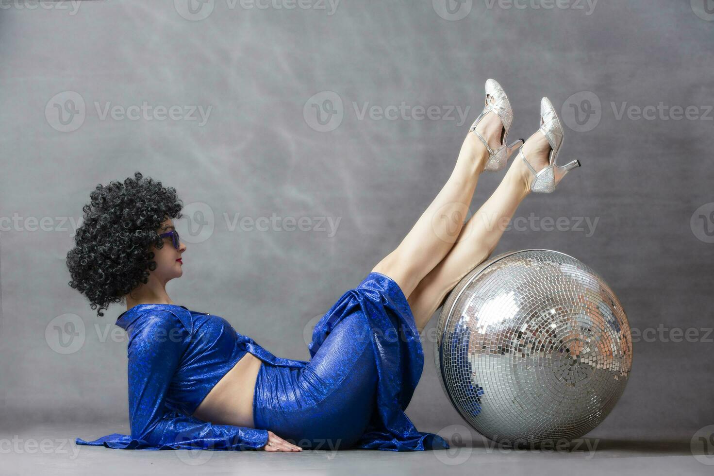 Girl with a disco ball in an afro wig on a gray background. Disco style from the seventies or eighties. photo