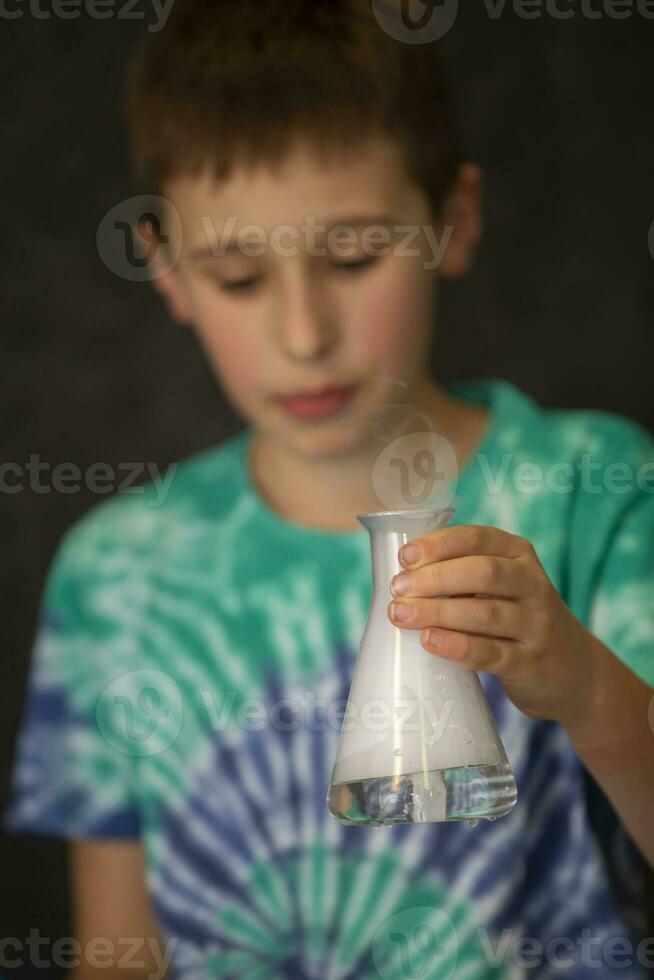 A boy conducts a scientific chemical experiment with liquid nitrogen. A child with a glass flask filled with smoke. photo