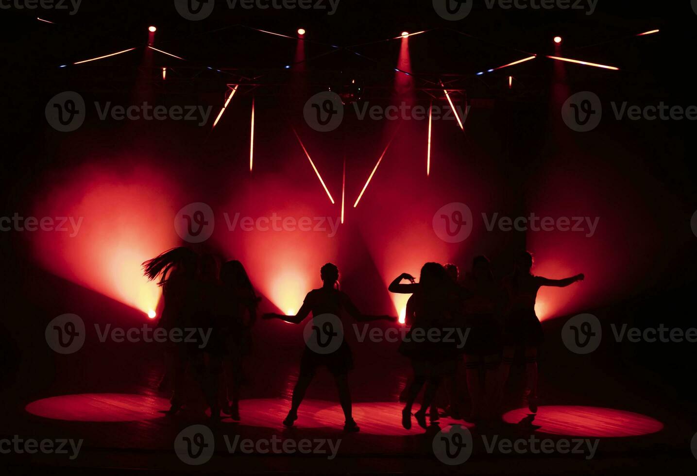 Dark silhouettes of dancing girls against the background of red light from stage spotlights. photo