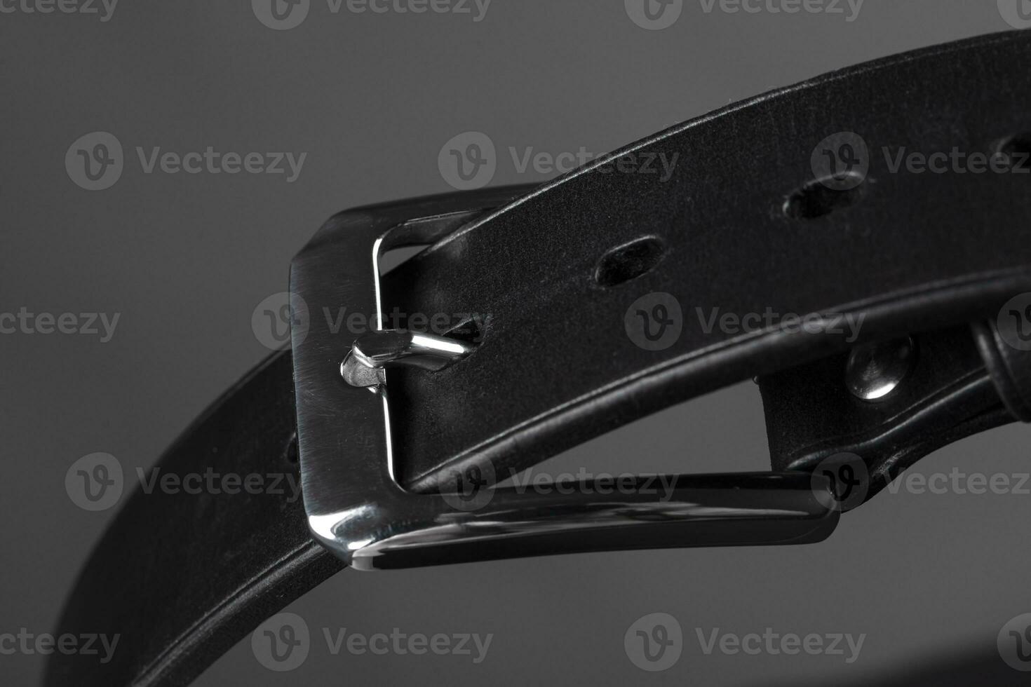 Part of a black leather belt with a metal buckle close-up on a gray background. photo