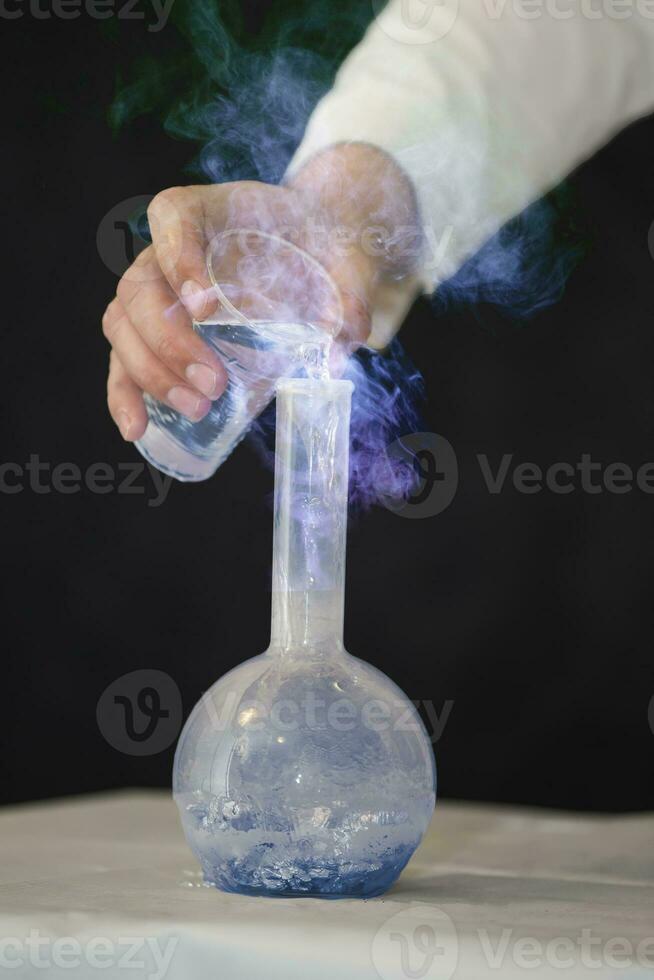 Chemist laboratory assistant pours a luminous mystical solution into a medical flask. photo