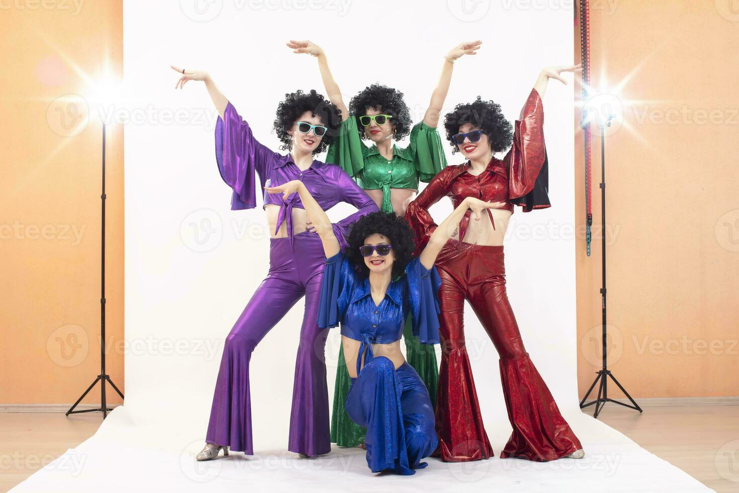 un grupo de muchachas en vistoso acampanado trajes y afro pelucas actitud en un foto estudio. disco estilo desde el ochenta o setenta