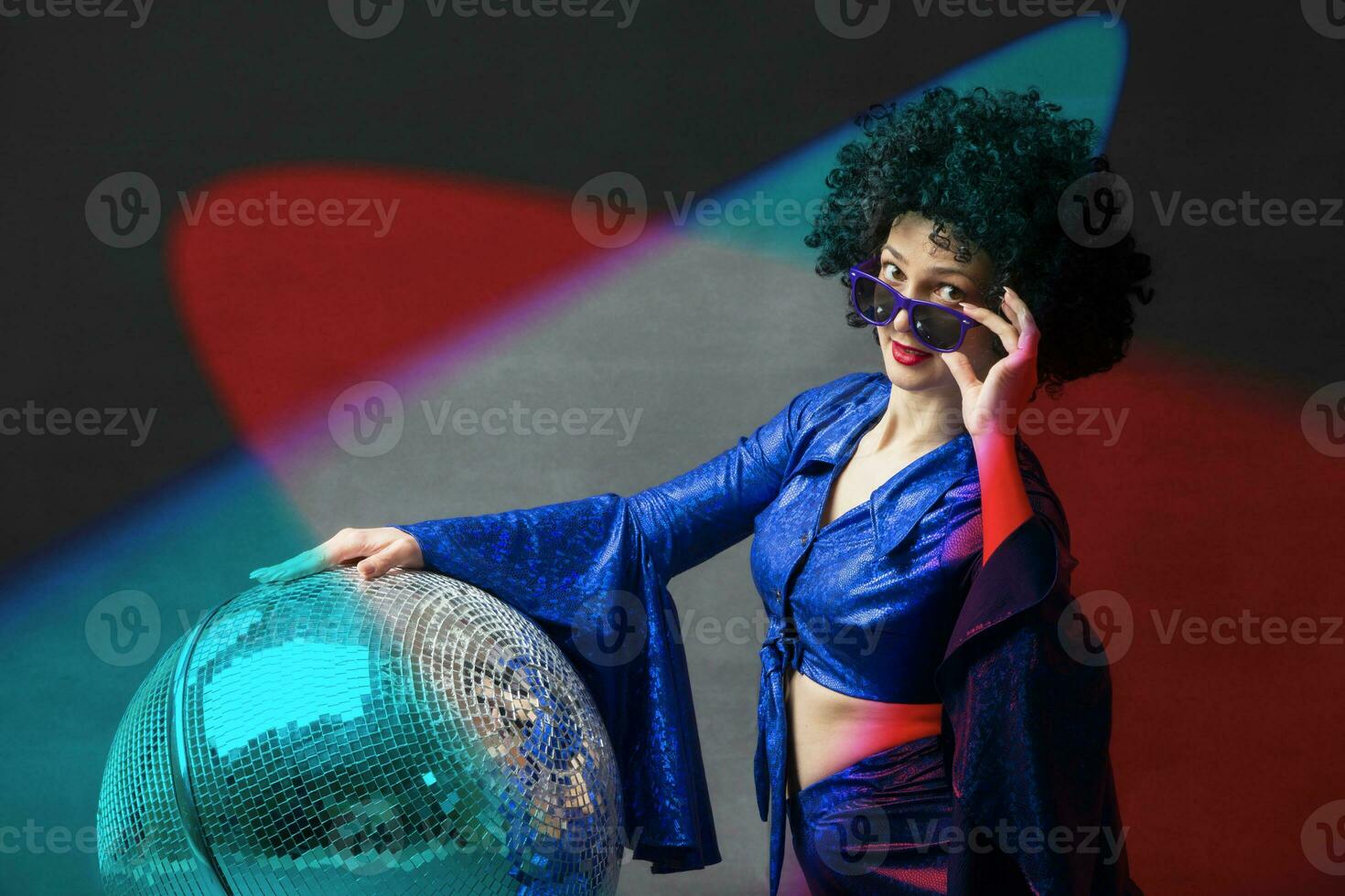 A woman with a disco ball in an afro wig in multi-colored rays of light. Disco style from the seventies or eighties. photo