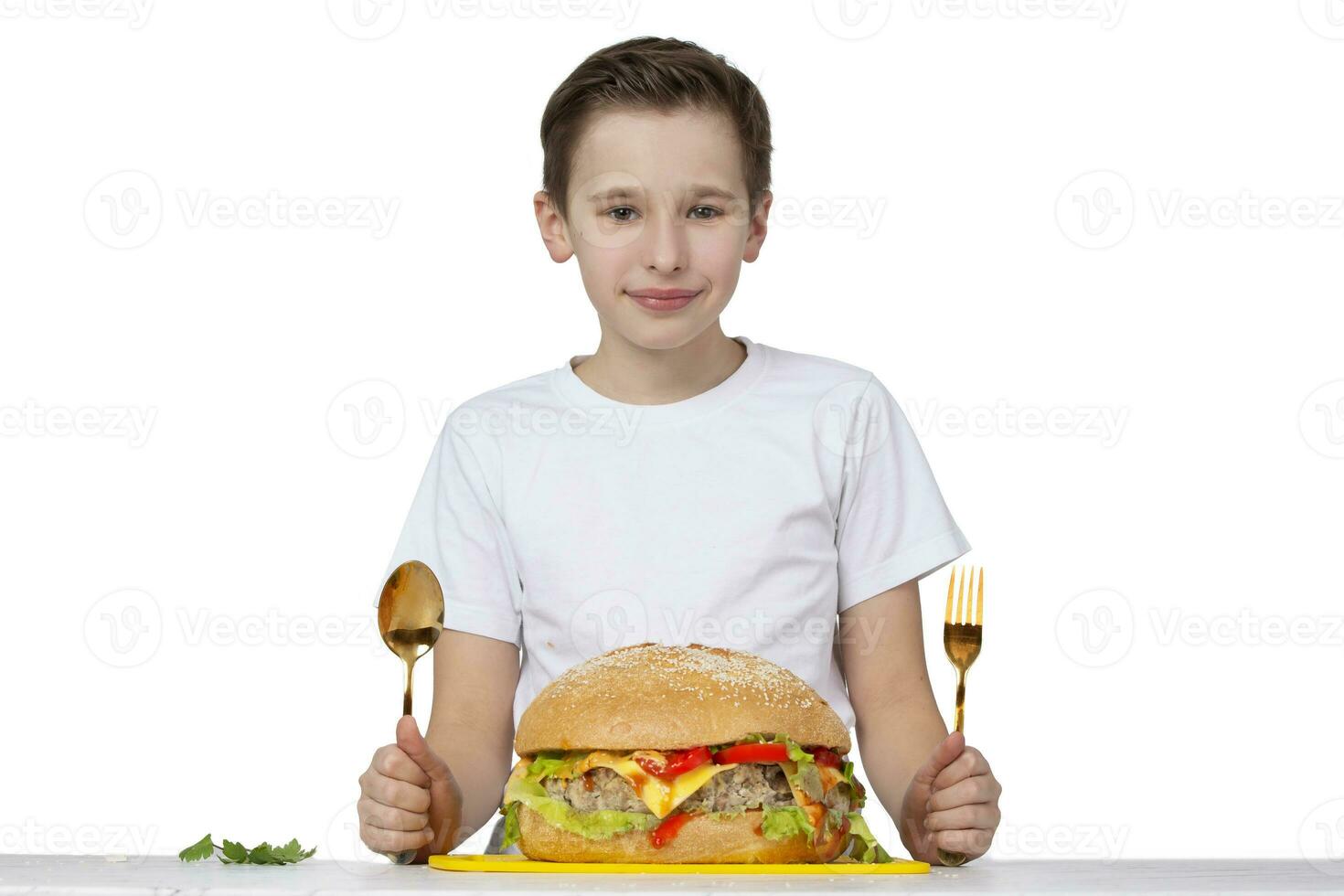 Young boy with big hamburger isolated in white. A teenager holds a golden fork and a spoon. photo